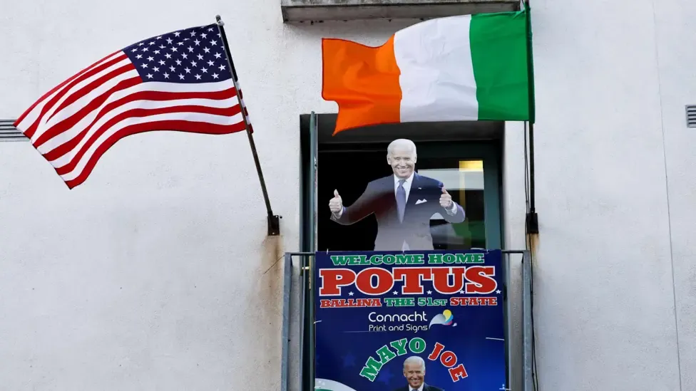 A cardboard cut-out of Joe Biden. Above the cut-out there is an Irish flag and an American flag. There is also a sign which reads 'WELCOME HOME POTUS'